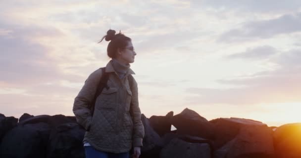 Mladá, vřele oblečená žena kráčí po pobřeží při západu slunce — Stock video