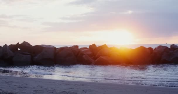 Μια νεαρή γυναίκα με ζεστά ρούχα περπατά κατά μήκος της ακτής το ηλιοβασίλεμα. — Αρχείο Βίντεο