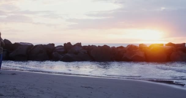 En ung varmt klädd kvinna går längs havskusten vid solnedgången — Stockvideo