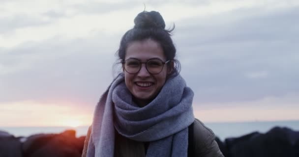 Μια νεαρή γυναίκα με γυαλιά γελώντας κοιτάζοντας την κάμερα στη θάλασσα. — Αρχείο Βίντεο