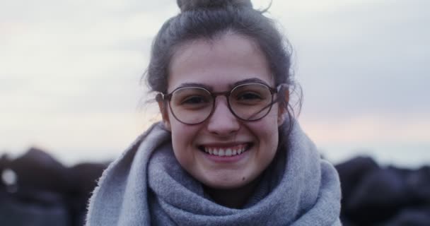 Młoda kobieta w okularach ze śmiechem patrząca w kamerę na wybrzeżu — Wideo stockowe