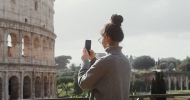 Genç bir kadın cep telefonuyla Colosseum 'un fotoğraflarını çekiyor.