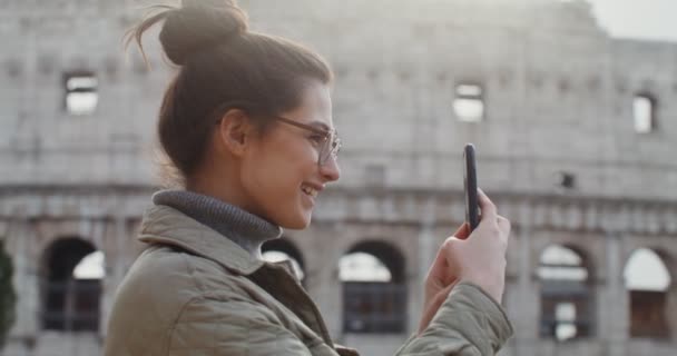 En ung kvinde tager billeder stående på et observationsdæk nær Colosseum – Stock-video