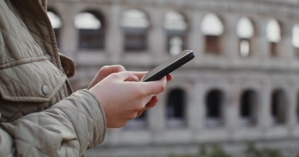 Женщина набирает сообщение на мобильный телефон, стоя перед Колизеем — стоковое видео