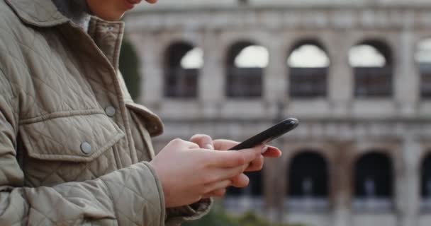 Uma mulher marca uma mensagem no telemóvel enquanto está em frente ao Coliseu — Vídeo de Stock
