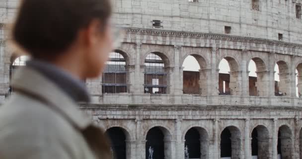 Egy fiatal, gyönyörű nő nézi a Colosseumot, ahogy a kilátófedélzeten áll. — Stock videók