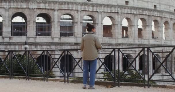 Een jonge vrouw komt naar het observatiedek voor het Colosseum en kijkt — Stockvideo