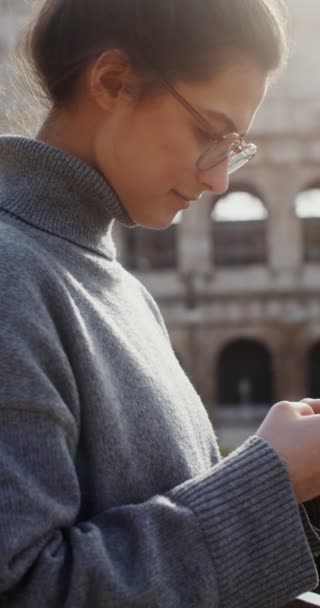 Egy nő tárcsáz egy üzenetet a mobilján, miközben a Colosseum előtt áll. — Stock videók