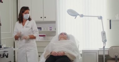 Bir kozmetolog hastanın yüzüne tıbbi hazırlıklar yapar.