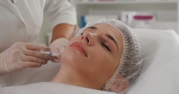 एक प्रसाधन सामग्री विशेषज्ञ चिकित्सा तैयारी के साथ रोगी के चेहरे का इंजेक्शन बनाता है — स्टॉक वीडियो