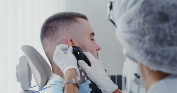 Ein Hals-Nasen-Ohren-Arzt untersucht die Ohrmuschel eines Patienten mit einem medizinischen Spiegel — Stockvideo