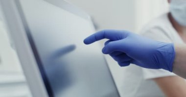 Hijyenik eldivenli bir doktor tablet kullanır ve parmağını ekranda gezdirir.