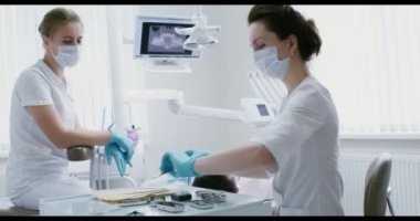 Bir dişçi kadın aletleri alır ve hastaların ağız boşluklarını muayene eder.