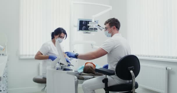 Zubař upevňuje pečeť ultrafialovou září, mladá sestra pomáhá — Stock video