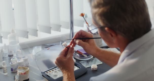 Gros plan sur la peinture d'une couronne dentaire en céramique avec un pinceau fin à la main — Video