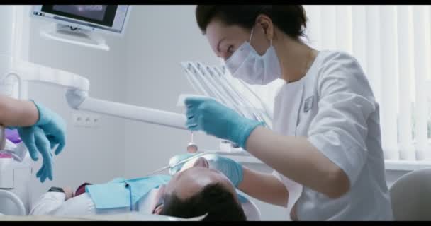 En kvinnlig tandläkare undersöker munhålan hos en patient som ligger på en tandstol — Stockvideo