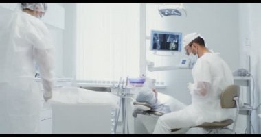 Hemşire çalışma aletlerini hazırlarken bir dişçi bir hastayla konuşuyor.