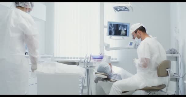Un dentista está hablando con un paciente mientras una enfermera está preparando herramientas de trabajo — Vídeo de stock