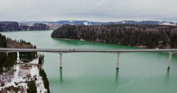 Quadcopter βίντεο από μια γέφυρα κατά μήκος ενός ποταμού στους λόφους που καλύπτονται από χιονισμένο δάσος. — Αρχείο Βίντεο