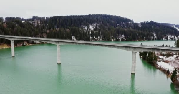 Quadcopter videó egy hídról a folyón keresztül a hegyekbe borított havas erdő. — Stock videók