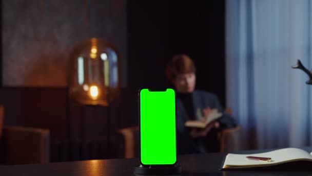 Un mobile con uno schermo verde sta su desktop di donna d'affari che legge un libro — Video Stock