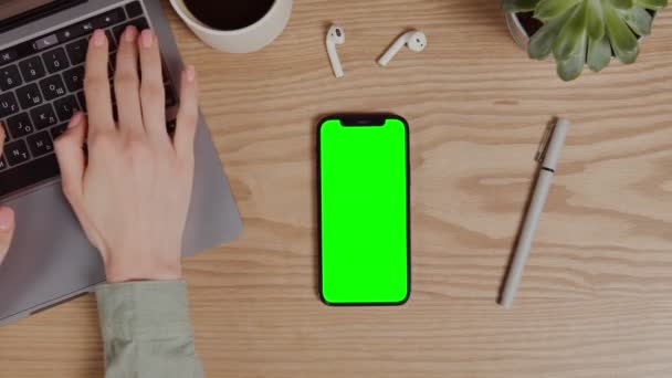Ένα κινητό τηλέφωνο με πράσινη οθόνη βρίσκεται στην επιφάνεια εργασίας δίπλα σε ένα φορητό υπολογιστή — Αρχείο Βίντεο