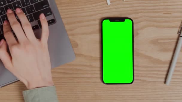 Un teléfono móvil con una pantalla verde se encuentra en el escritorio junto a un ordenador portátil — Vídeos de Stock