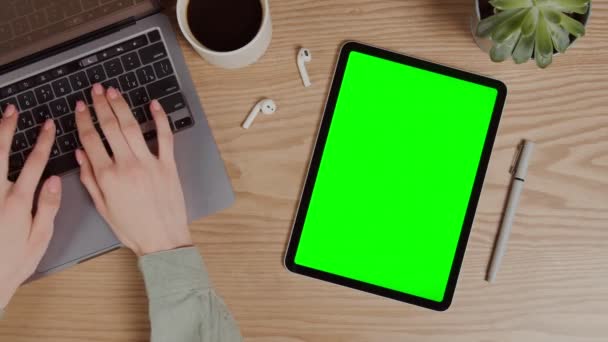 Tablet digital com uma tela verde deitada em uma mesa ao lado de digitar mãos femininas — Vídeo de Stock