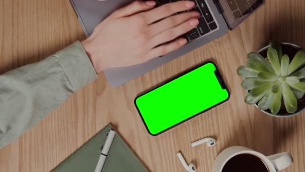 Un teléfono móvil con una pantalla verde se encuentra en el escritorio junto a un ordenador portátil — Vídeo de stock