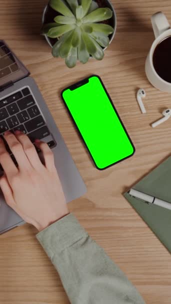 Мобільний телефон з зеленим екраном лежить на робочому столі поруч з ноутбуком — стокове відео