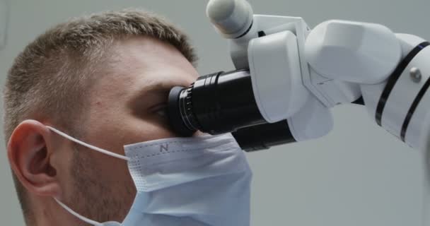 Врач или ученый в медицинской маске смотрит в микроскоп — стоковое видео