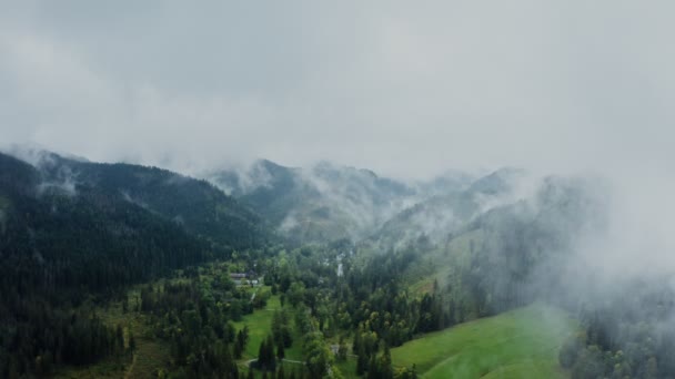Um vale de montanha verde com casas em uma planície entre montanhas inclinadas — Vídeo de Stock