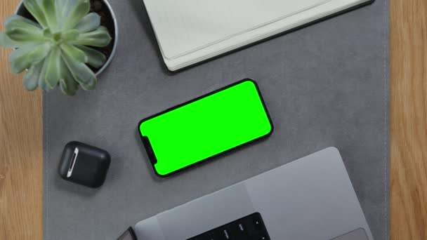Αρσενικά χέρια βάζοντας ακουστικά δίπλα στο κινητό τηλέφωνο με πράσινη οθόνη στην επιφάνεια εργασίας — Αρχείο Βίντεο