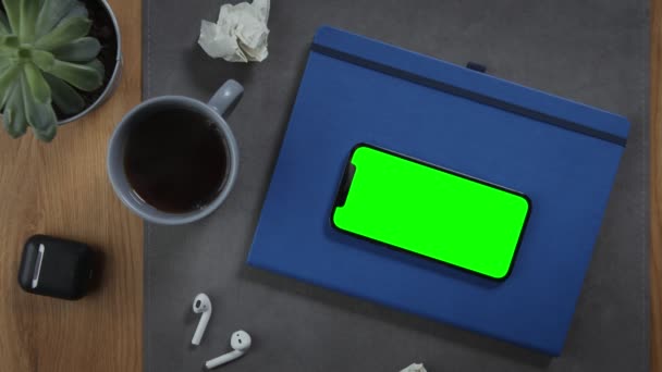Un teléfono móvil con una pantalla verde se encuentra en un bloc de notas en el primer plano del escritorio Fotografías de stock