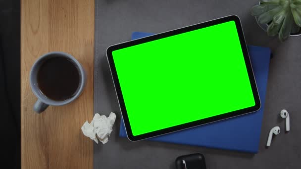 Ένα tablet με μια πράσινη οθόνη βρίσκεται στην επιφάνεια εργασίας δίπλα σε ένα φλιτζάνι ζεστό τσάι — Αρχείο Βίντεο