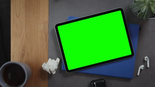 A man puts cup of tea on the desktop next to a tablet with a green screen — Stock Video