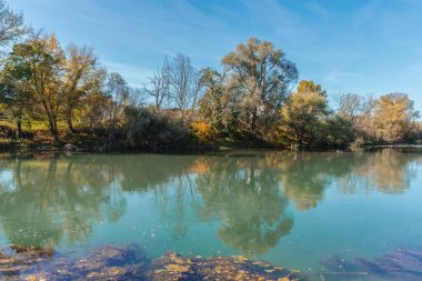 Banja Luka 'daki güzel nehir mavi ve gri bulutlu gökyüzü ve sudaki ağaç yansıması