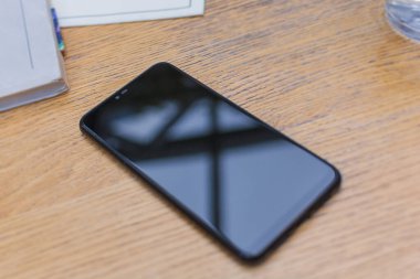 Boş ekran defteri olan siyah cep telefonu ahşap masa üzerinde tasarım oluşturur