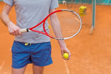Turuncu tenis kortunda raket ve sarı top tutan tenisçi.