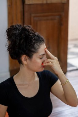 Güzel bir genç kadının portresi, gözleri kapalı oturuyor ve eli alnında, goya yapıyor ve evde meditasyon yapıyor..