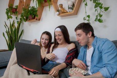 Üç genç arkadaş, bir erkek ve iki kız, dizüstü bilgisayarda çizgi film izliyorlar..