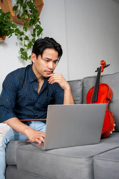 Young Hispanic man, music student, watching lessons on the laptop