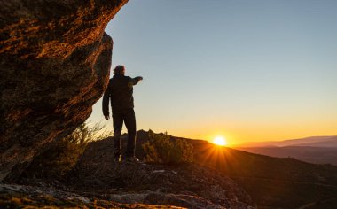 Güneş ufukta doğarken insan silueti dağ kayaları üzerinde bir kontaluz.