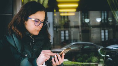 Merdivende oturan bir kadın telefona bakıyor.