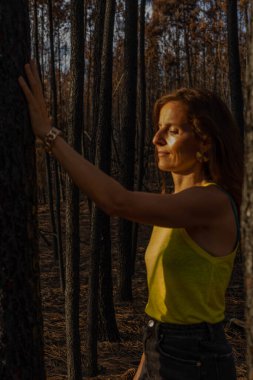 woman touches with her hand a tree that is part of a devastated forest