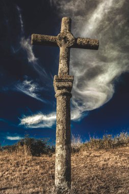 stone cross at sunset with a sky with clouds and the ground with dry grass
