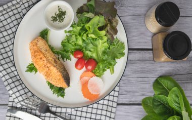 Ahşap masa manzaralı organik sebzeli kızarmış somon bifteği.