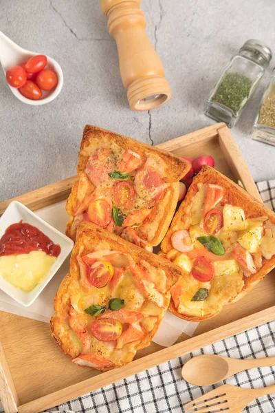 Pizza bread topped with shrimp, crab sticks, tomatoes, sausage, cheese in a wooden tray with sauce top view