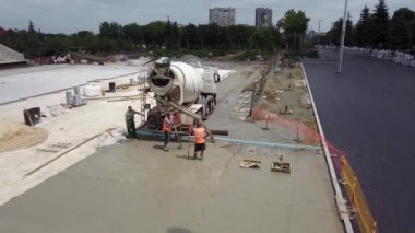 Ukrayna, Mariupol - 1 Eylül 2020. Kostruction sahasına yeni şehir meydanının beton taraması için hazır karışık bina karışımı döken çimento karıştırıcı hava aracı. Hatta yüzeyi tarayan işçiler.