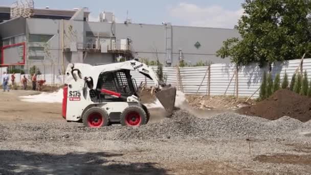 Ukraine, Mariupol - September 1, 2020. Small skid steer loader moving gravel and soil on construction site. Mini loader doing earthwork excavating flat surface for square area bedding. — Stock Video